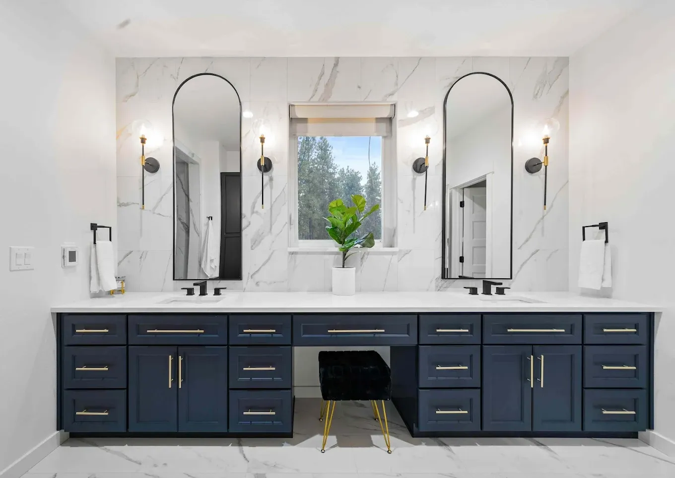 A bathroom with navy blue cabinets, double vanity and sinks, and white and gray marbled walls