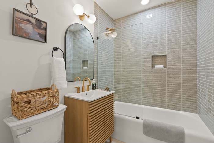A white bathroom with a combination shower bathtub with gray tile walls.