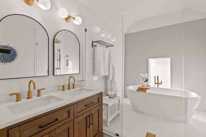 A white bathroom with brown cabinets, double vanity, and large soaking bathtub.