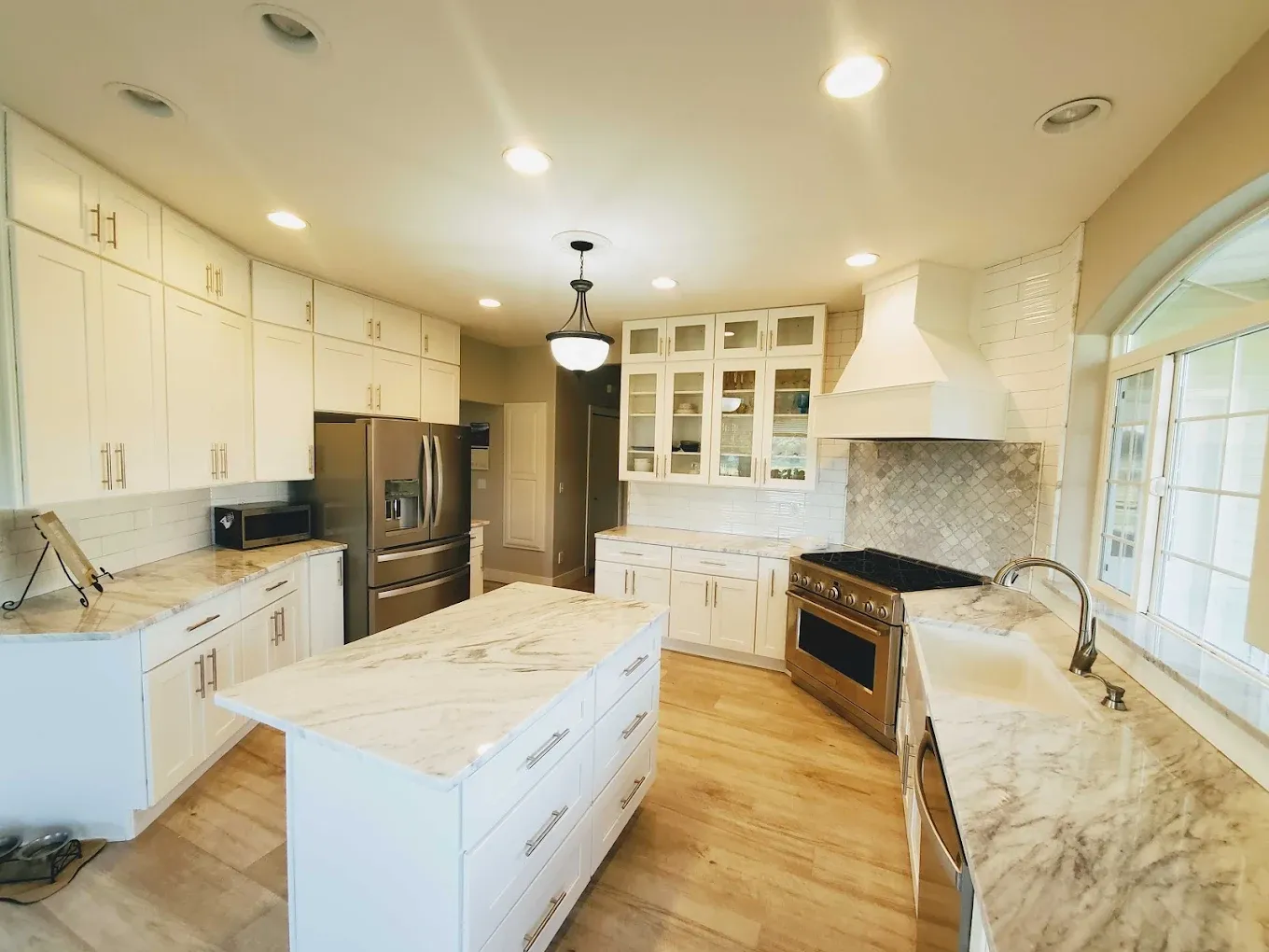 A kitchen with white cabinets, white and gray marbled countertops, and large central island.