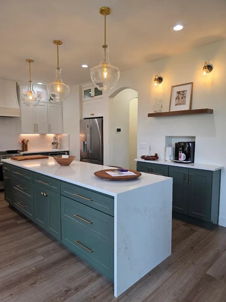 A kitchen with green cabinets and a central island with white waterfall stone countertop.