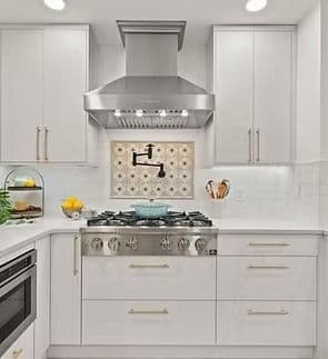 A kitchen with white cabinets and gold fixtures, stainless steel appliances, and tile backsplash.