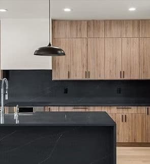 A kitchen with natural brown cabinets and black stone marbled backsplash and waterfall style island.